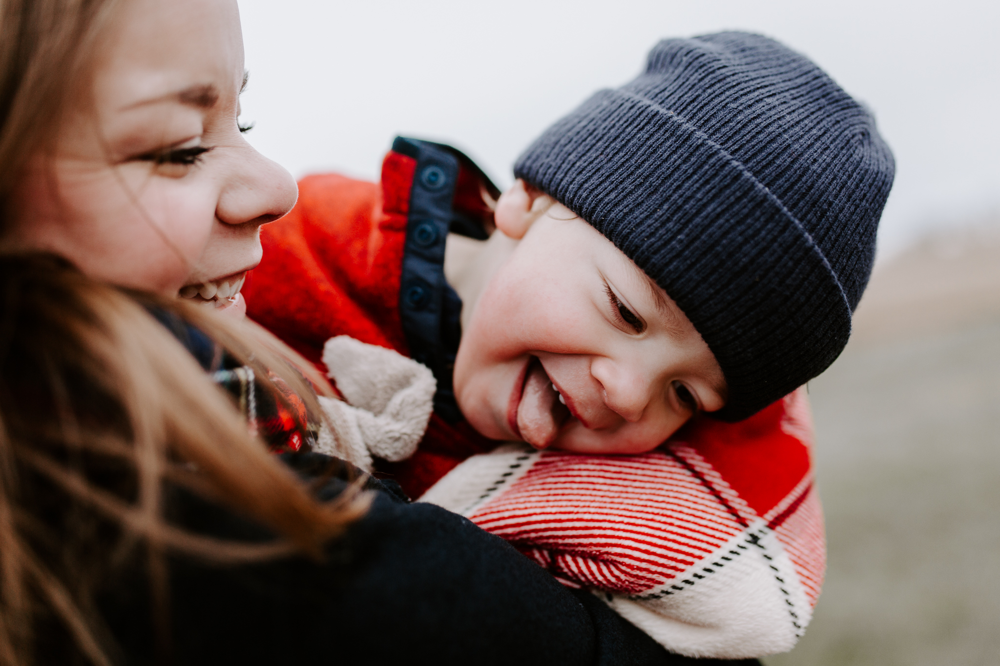 Mother in a plaid scarf swinging her young boy in her arms.